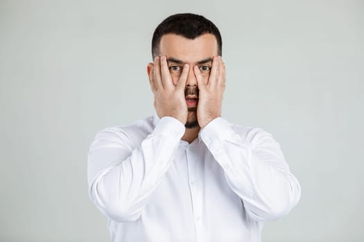 portrait of handsome bearded man closes his eyes with hand on gray background