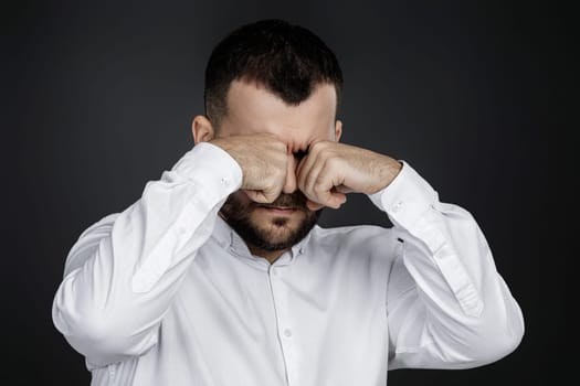 portrait of funny bearded man is crying and wiping tears on black background.