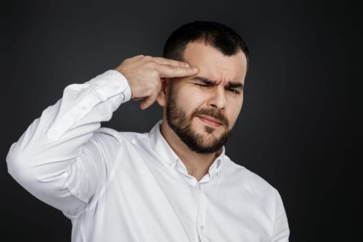 bearded man in white shirt shooting in temple with hand on black background.