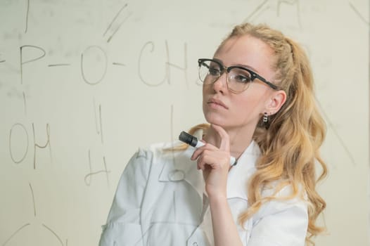 A Caucasian woman in a medical gown thinks and finalizes formulas on a transparent wall