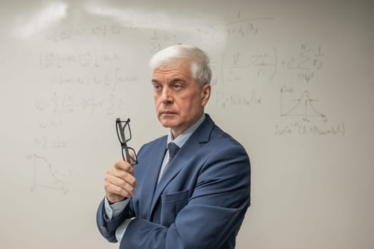 Mature man stands at a white board with written formulas