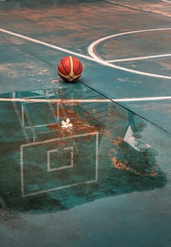 Basketball backboard and hoop with reflection water after rain and Basketball ball on outdoor court. Basketball on wet court, Basketball half-court line, Space for text, Selective focus.