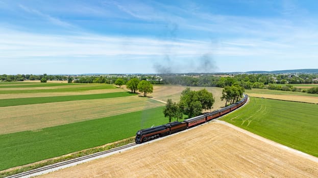 A captivating aerial shot of a steam train gliding through a green rural panorama, weaving between fields and emitting a trail of smoke against a clear sky