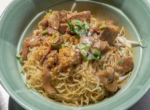 Egg Noodles with Braised pork (stewed pork) and Mung bean sprouts without Soup sprinkled with Coriander, Chopped onions and pepper in Green ceramic bowl. Selective focus.