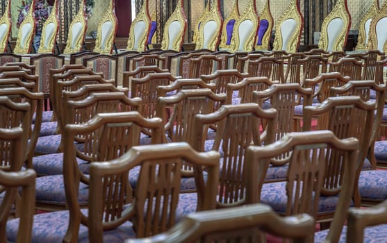 Bangkok, Thailand - May 22, 2024 - Perspective view of Wooden chairs with cushion seat and Pulpit within Samphanthawong Saram Worawihan temple. Space for text, Selective focus.