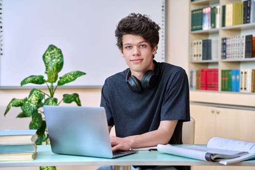 Portrait of college student guy sitting at desk with laptop computer and textbooks inside educational library classroom. Education internet technology e-learning learning services applications youth