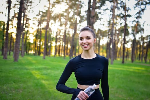 Young woman in tracksuit smiling holding a water bottle getting ready for a sport in the forest