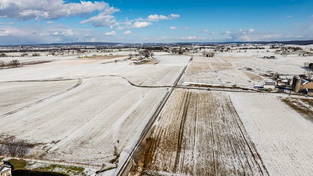 An Aerial View Of Vast Snow-Dusted Farmland With Sparse Buildings And Roads.