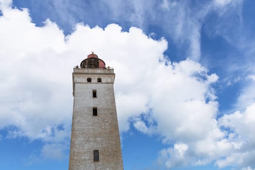 Tourists walk on the sand near the Rubjerg Knude Lighthouse on the coast of the North Sea in the Jutland in northern Denmark. Natural landscape with sand dunes. Rubjerg, Denmark - August 24, 2023.