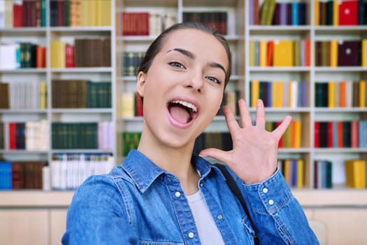 Selfie photo portrait of smiling cool happy cheerful high school student girl, inside library of educational building. Education, adolescence, lifestyle concept