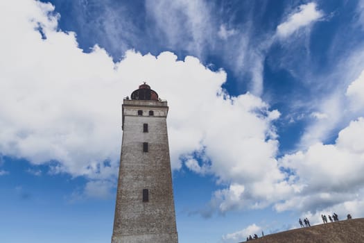 Tourists walk on the sand near the Rubjerg Knude Lighthouse on the coast of the North Sea in the Jutland in northern Denmark. Natural landscape with sand dunes. Rubjerg, Denmark - August 24, 2023.