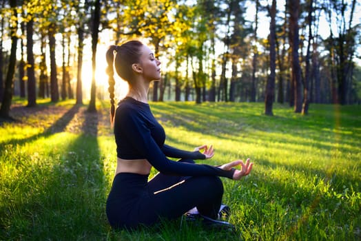 A young woman practices meditation in a serene forest during sunrise, promoting peace and mindfulness.
