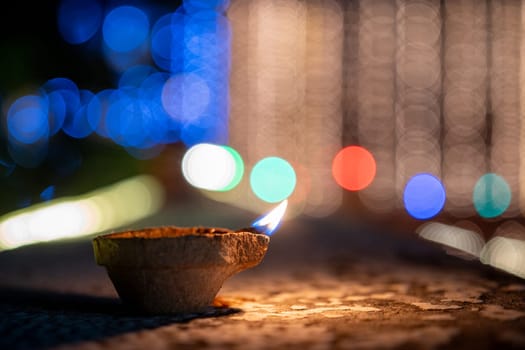 handmade earthenware clay coconut fiber diya lamp lit in front of the soft focussed bokeh lights of diwali major celebration in India