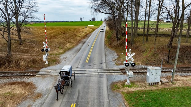 A Rural Road with An Amish Horse-Drawn Carriage at Railroad Crossing