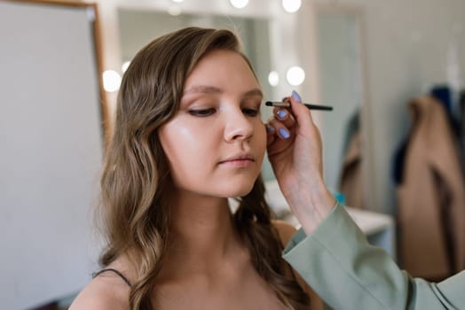 Backstage of photo shoot: Make-up artist applies makeup on beautiful white model.