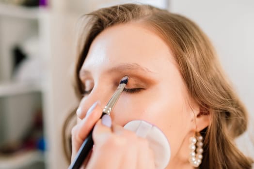 Backstage of photo shoot: Make-up artist applies makeup on beautiful white model.