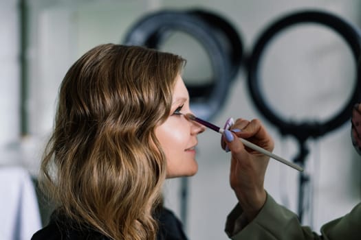 Backstage of photo shoot: Make-up artist applies makeup on beautiful white model.