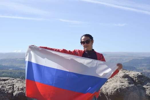 The Russian flag is on the shoulders of a girl standing against the backdrop of the Caucasus mountains. Unity Day in Russia