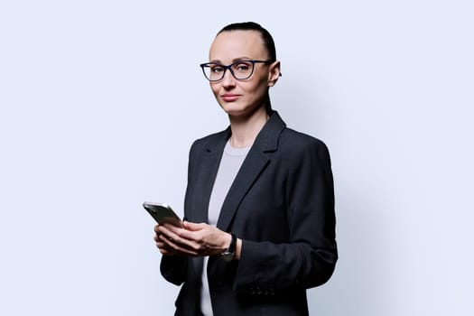 Adult smiling woman holding smartphone on white background. 30s female looking at camera with phone in hands. Technologies mobile applications internet work business leisure communication