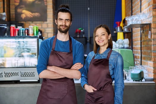 Small business team portrait of confident successful colleagues partners young man woman in aprons posing looking at camera at workplace in restaurant coffee shop cafeteria. Partnership teamwork work