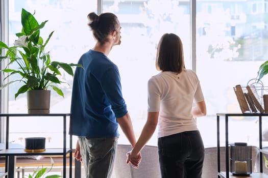 Back view, silhouette of young couple holding hands looking out window. Love friendship romance relationship, happiness, lifestyle, people concept