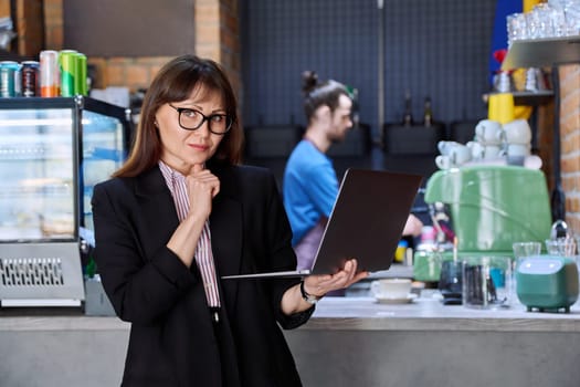 Portrait of confident business woman accountant financier lawyer small business owner. Successful middle-aged female using laptop computer looking at camera background coffee shop cafeteria restaurant