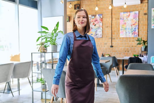 Attractive successful young woman service worker, business owner in apron in restaurant cafeteria coffee pastry shop interior. Small business staff occupation entrepreneur work