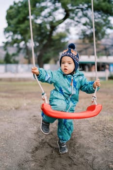 Little girl is standing, leaning her knee on a rope swing. High quality photo