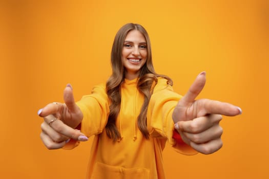 Young woman over yellow background points finger at you in studio
