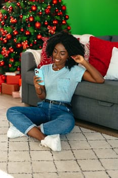 Happy black woman using smartphone in a room decorated for Christmas close up