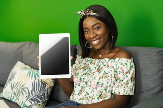 Young African woman using digital tablet while resting at home on sofa