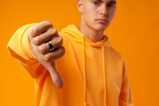 Young man showing a sign of dislike against yellow background close up