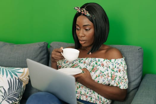 Young african woman working on laptop computer at home sitting on sofa close up