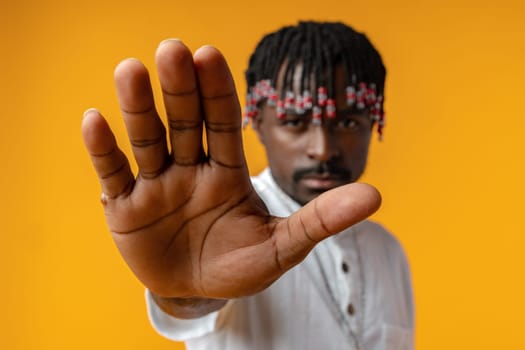 Portrait of serious African male showing hand stop sign on yellow background, close up