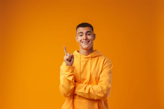 Handsome young man pointing to copy space on a yellow background in studio