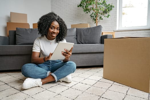 Young African woman using a tablet as she sits in living room surrounded by cardboard boxes close up