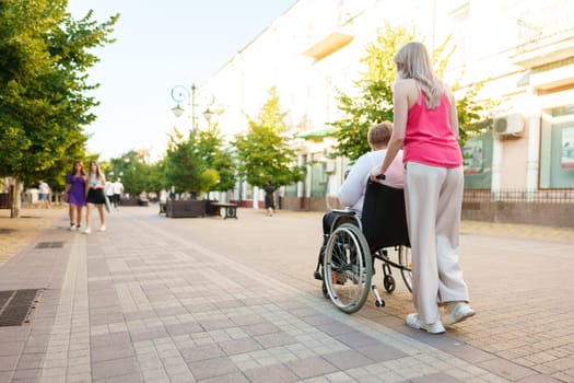 Young female caregiver pushing wheelchair with mature female person with disability across city street