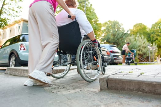 Young female caregiver pushing wheelchair with mature female person with disability across city street