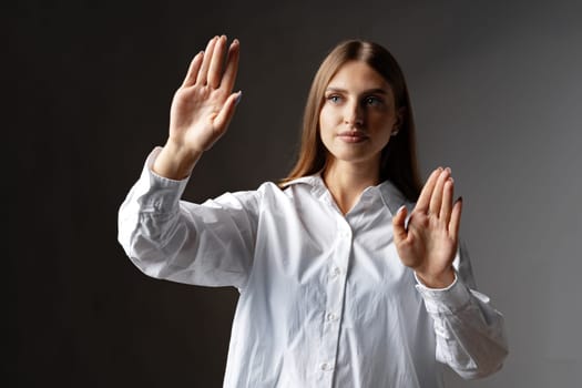 Young female entrepreneur touching virtual screen against grey studio background, close up