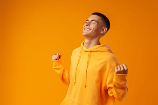 Portrait of a happy young man celebrating success against yellow background in studio