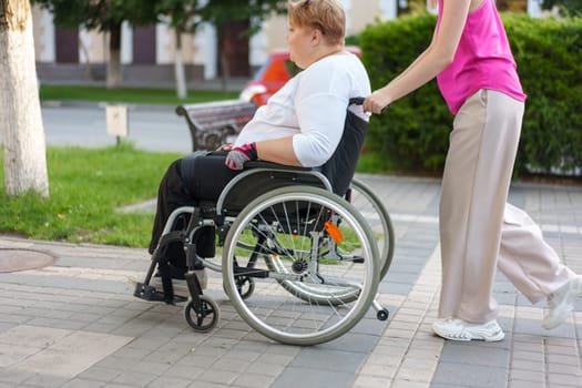 Young female caregiver pushing wheelchair with mature female person with disability across city street