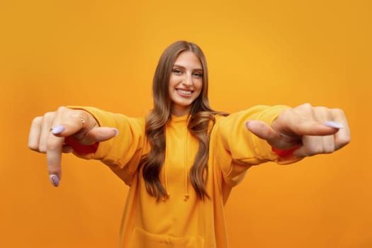 Young woman over yellow background points finger at you in studio