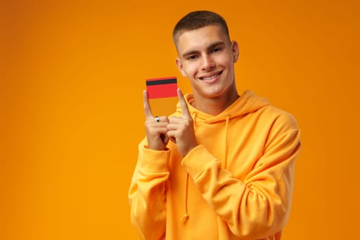 Handsome young man holding credit card on yellow color background in studio