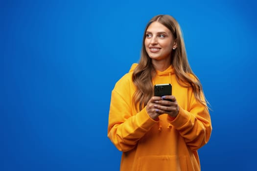 Portrait of young beautiful woman texting on the phone against blue background in studio