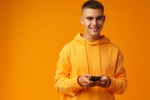 Portrait of a smiling young man holding mobile phone on yellow background, close up