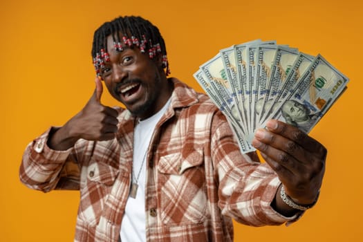 Young happy rich african man in casual shirt holding dollar bills against yellow background close up