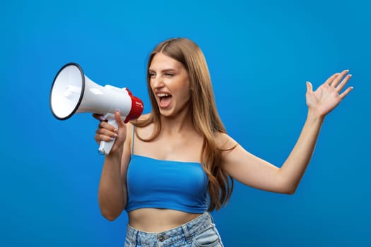 Young pretty woman with a megaphone against blue background in studio, close up