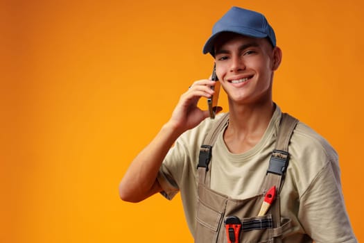 Young builder talking on a mobile phone against yellow background in studio