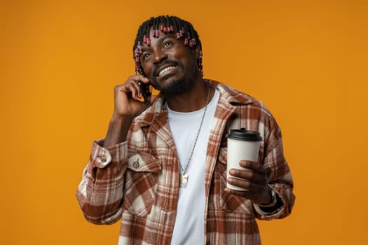 Cheerful african man talking on phone over yellow studio background close up