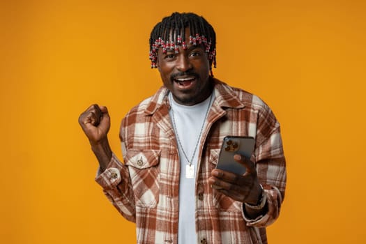 Young african man dressed in casual playing games on mobile phone over yellow background, close up